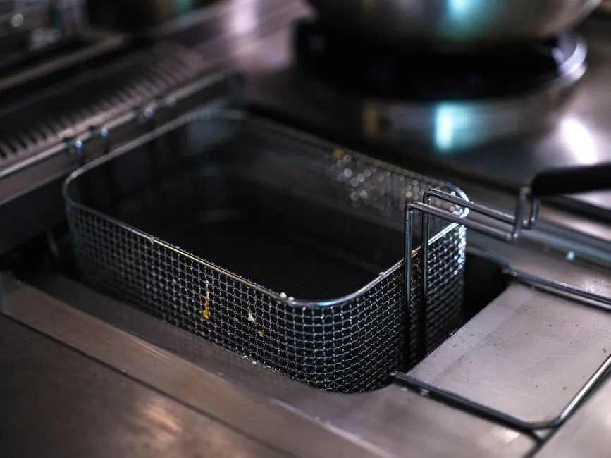 Empty fryer basket in an industrial kitchen, emphasizing cleanliness and hygiene.
